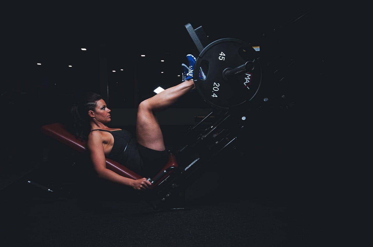 A member performing a leg press on a plate-loaded machine in a dimly lit gym